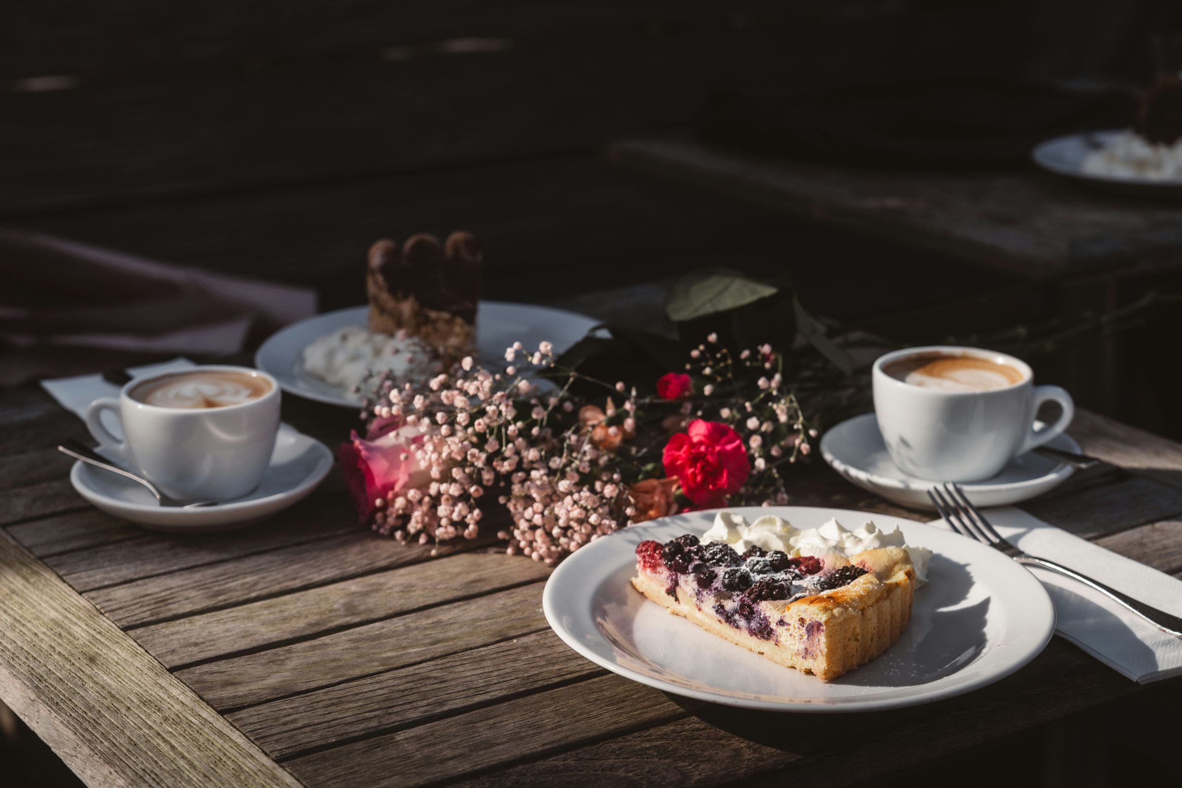Two cups of coffee and a slice of berry cake on a wooden table in morning light