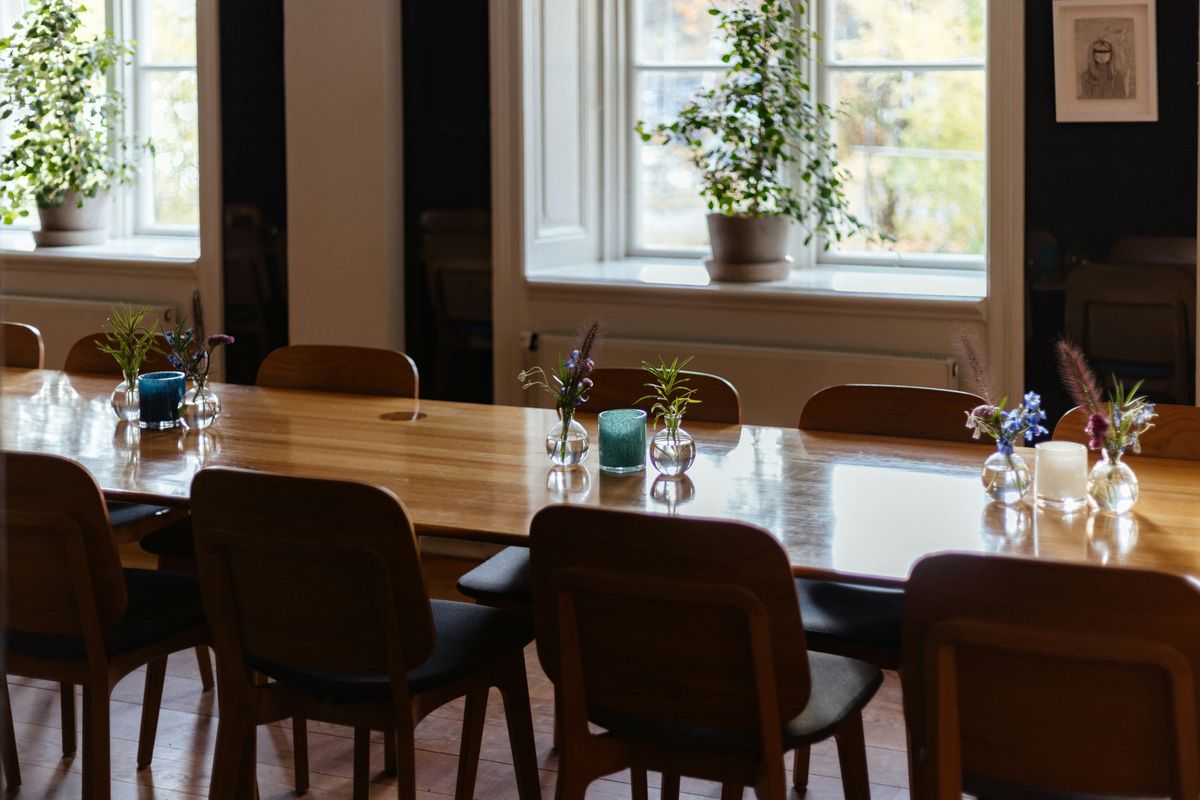 Empty room with a long wooden table, chairs and plants by the window